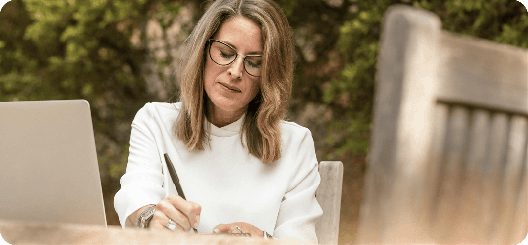 Žena středního věku, sedí venku a píše.
