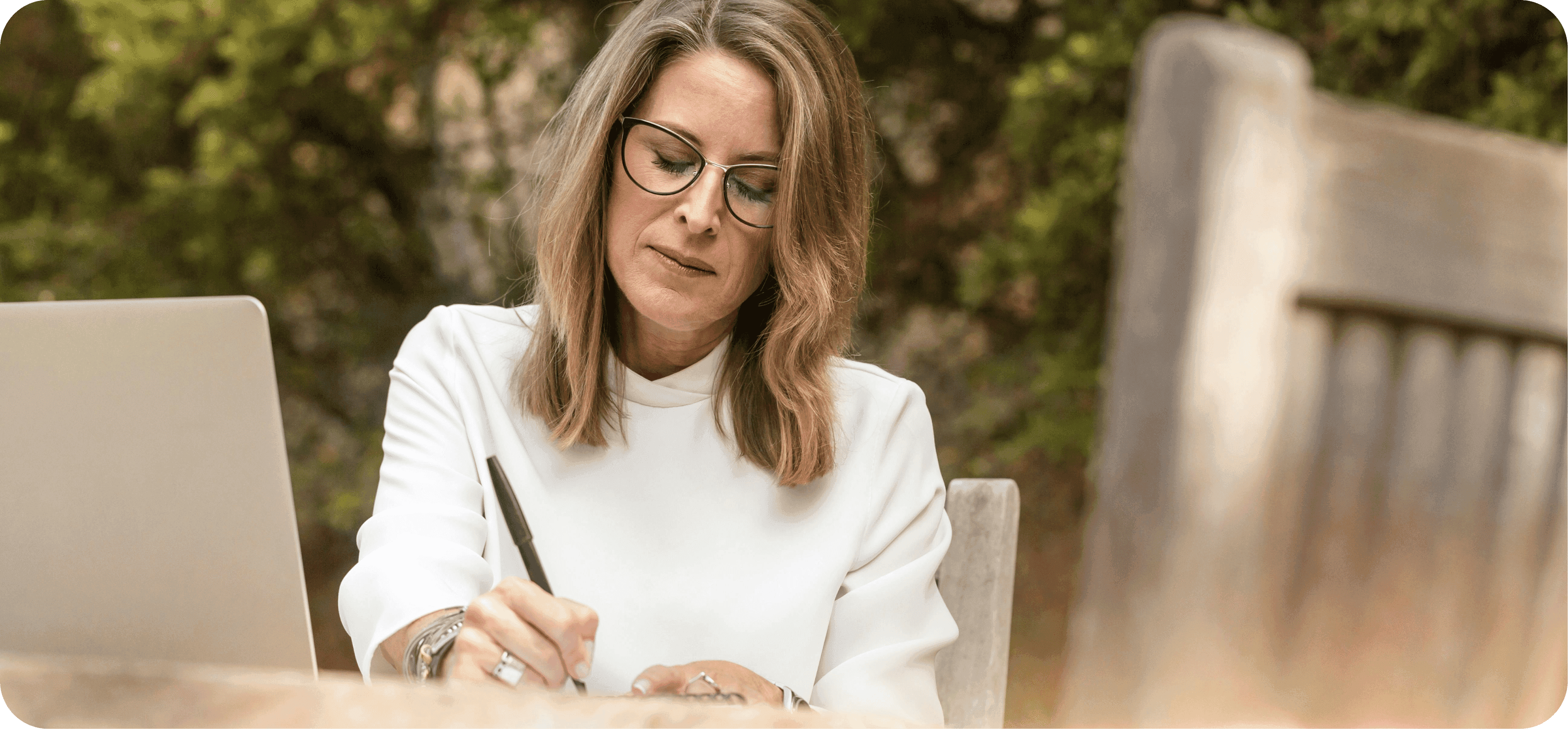Žena středního věku, sedí venku a píše.