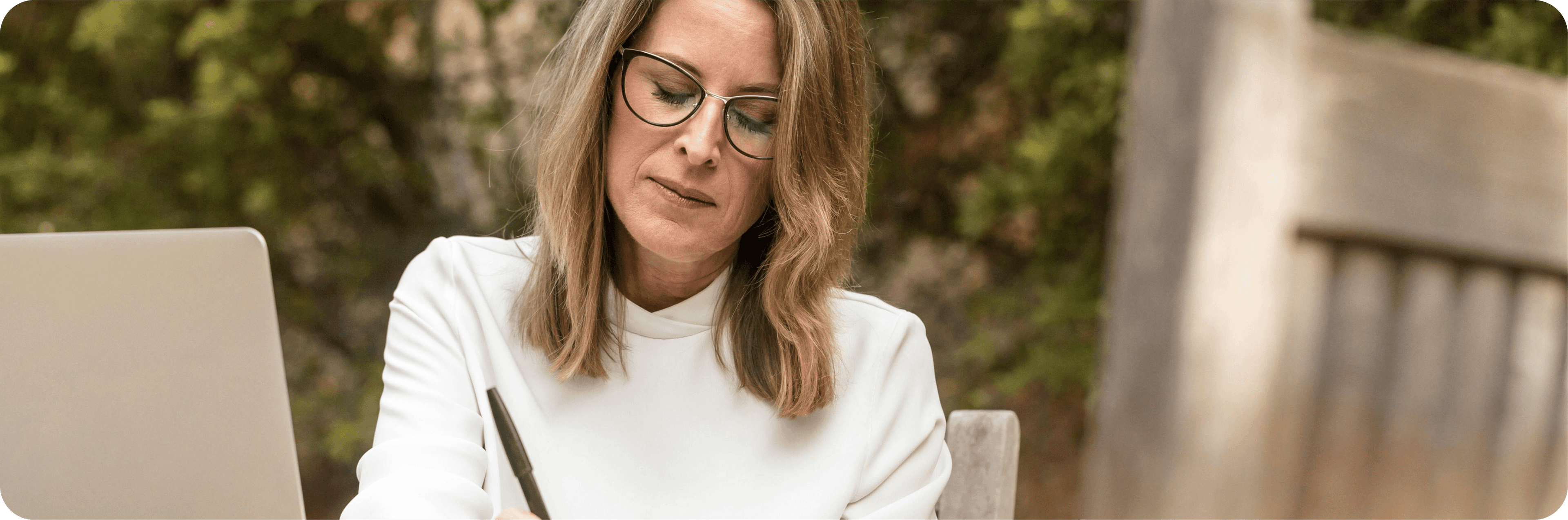 Žena středního věku, sedí venku a píše.