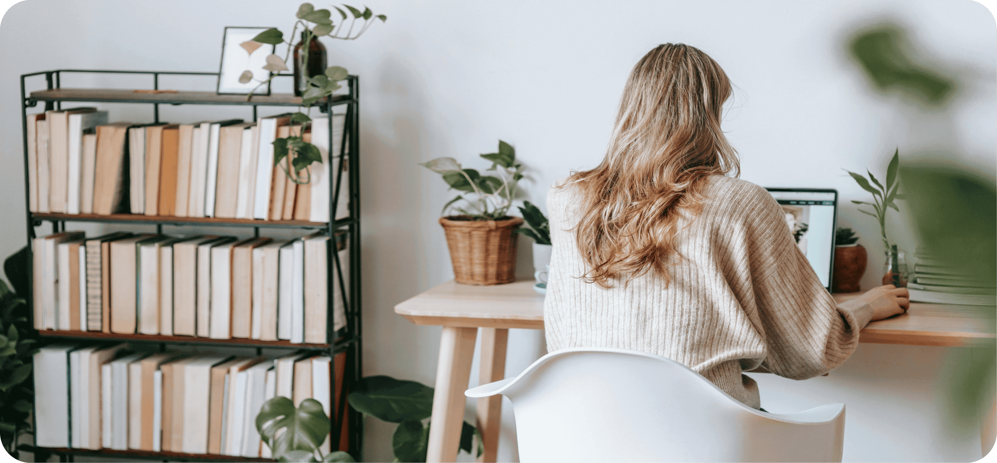 Žena sedící u notebooku vedle knihovny.