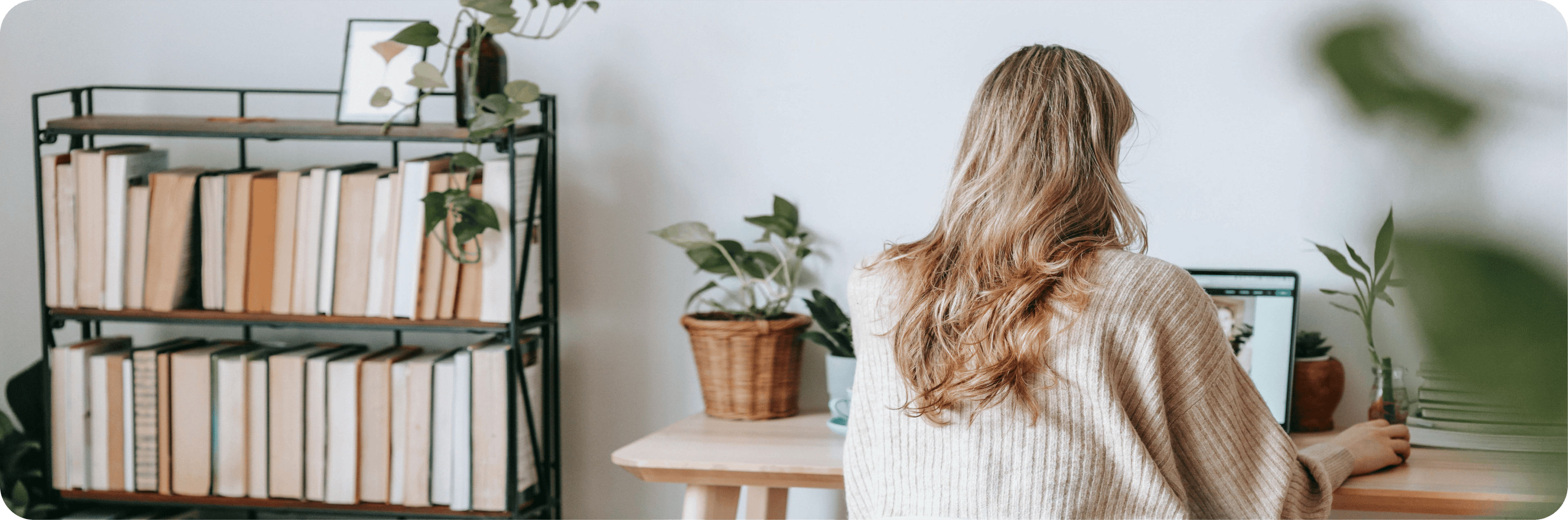 Žena sedící u notebooku vedle knihovny.